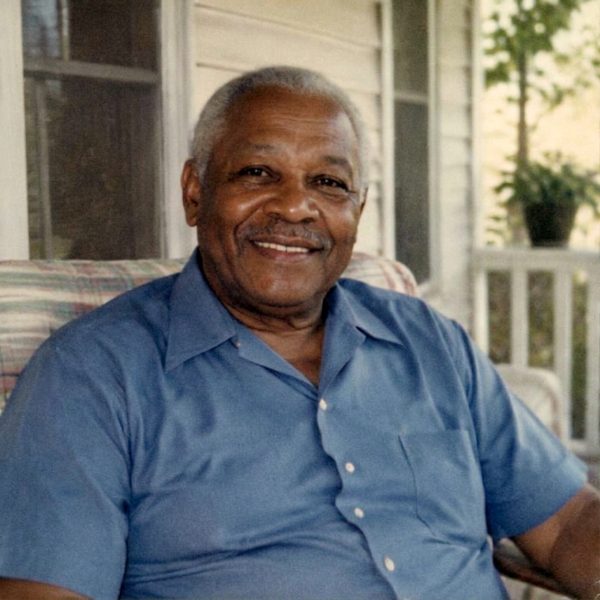 An older man smiling on a porch, restored